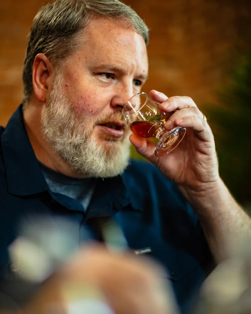 A bearded tastemaker taking a sip from a tasting glass