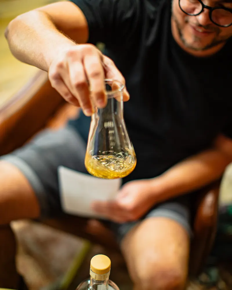 A tastemaker swirling bourbon in a glass flask over his scoring sheet